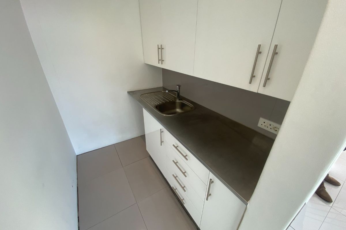 A compact, modern kitchenette featuring white cabinetry, a stainless steel countertop with an integrated sink, and tiled flooring.