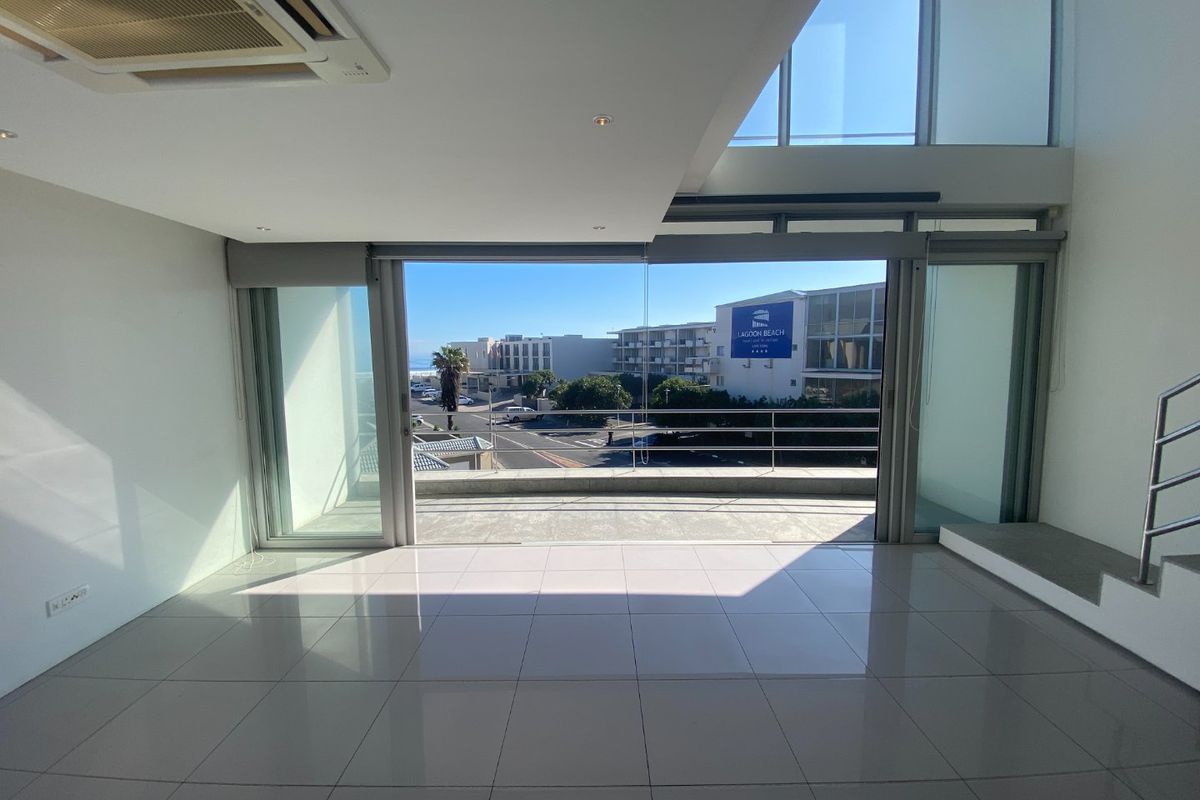 Bright and spacious open-plan living area featuring large sliding glass doors that open onto a balcony with coastal views.