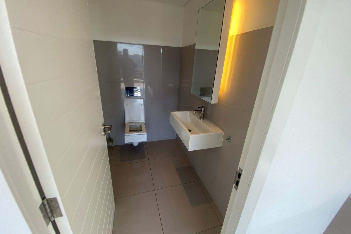 Modern commercial restroom featuring a wall-mounted basin, wall-hung toilet, and sleek tiled finishes with integrated mirror lighting.