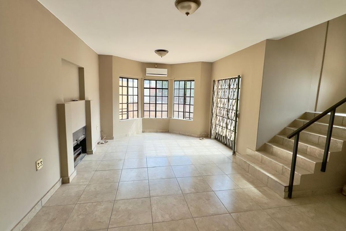 Spacious living area featuring tiled flooring, a built-in fireplace, bay windows, and an integrated staircase with a metal handrail.