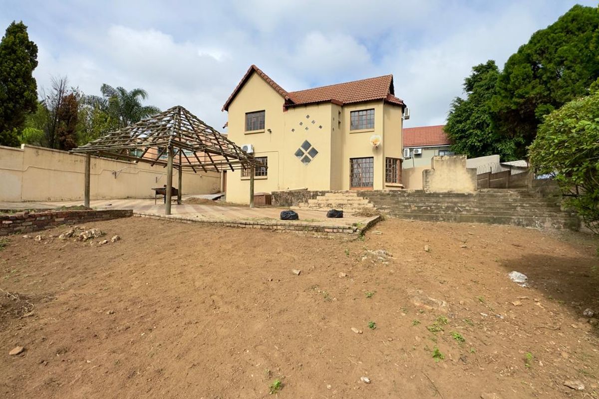 Rear view of the property featuring a large unlandscaped garden, a wooden pergola structure, and concrete stairs leading to the main house.