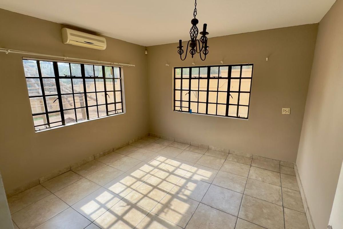 A bright, empty bedroom featuring tiled flooring, large windows with security bars, and a wall-mounted air conditioning unit.