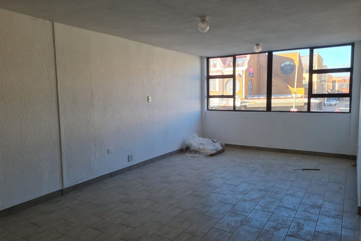 A bright, empty living area featuring large windows, tiled flooring, and textured walls, offering a versatile space ready for personalization.