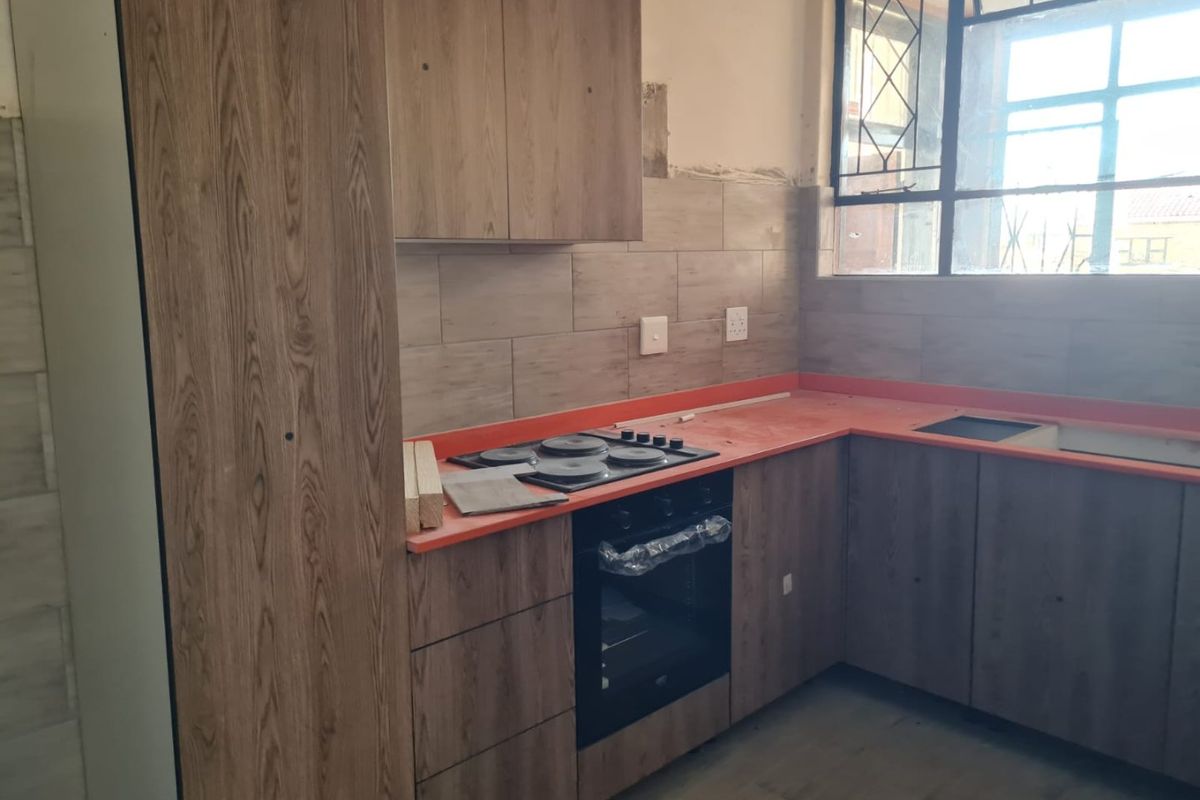 A kitchen featuring wood-look cabinetry, a built-in oven and hob, and a bright orange countertop, currently undergoing final finishing touches.