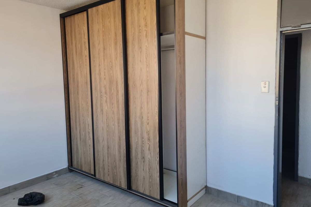 A bedroom featuring a modern built-in wardrobe with wood-grain sliding doors and black framing, set against a neutral interior.