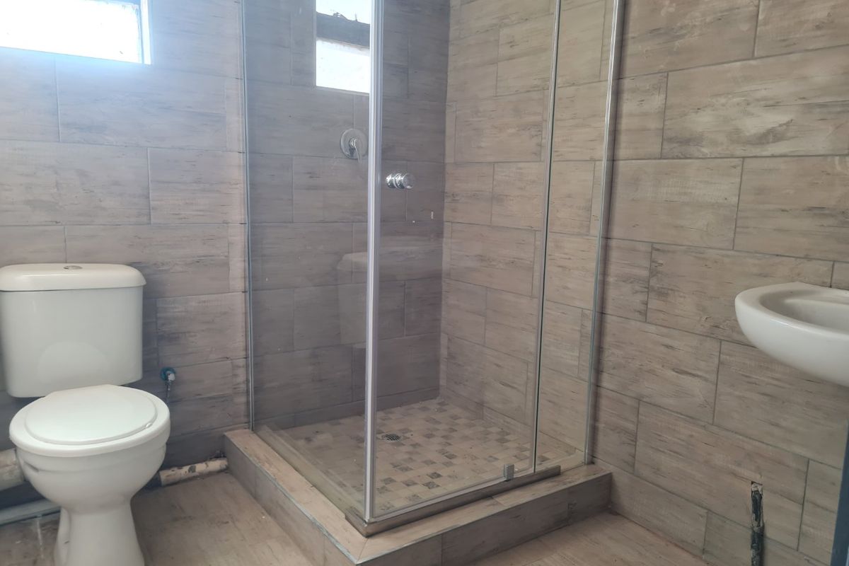 A functional bathroom featuring a glass shower enclosure, toilet, and wall-mounted basin with modern wood-look wall tiling.