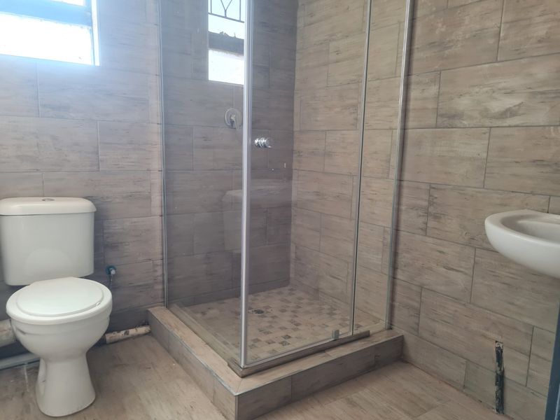 A functional bathroom featuring a glass shower enclosure, toilet, and wall-mounted basin with modern wood-look wall tiling.