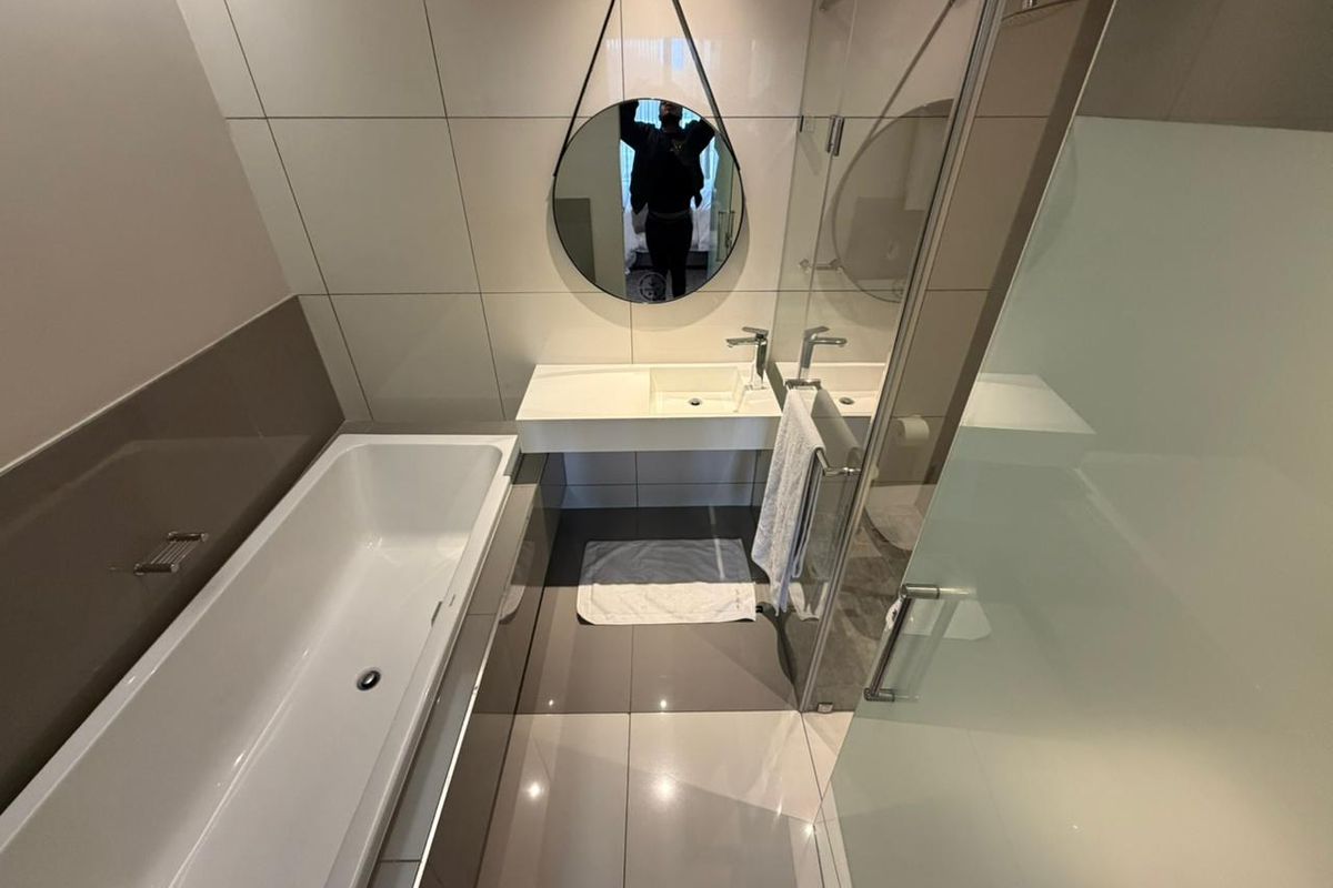 Modern bathroom featuring a sleek wall-mounted vanity, integrated basin, bathtub, and a glass-enclosed shower with contemporary tiling.