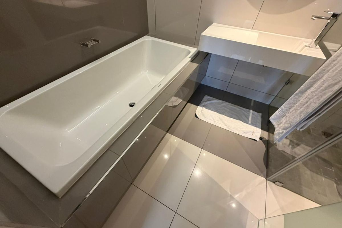 Modern bathroom featuring a built-in bathtub, wall-mounted vanity basin with chrome faucet, and large format floor and wall tiling.
