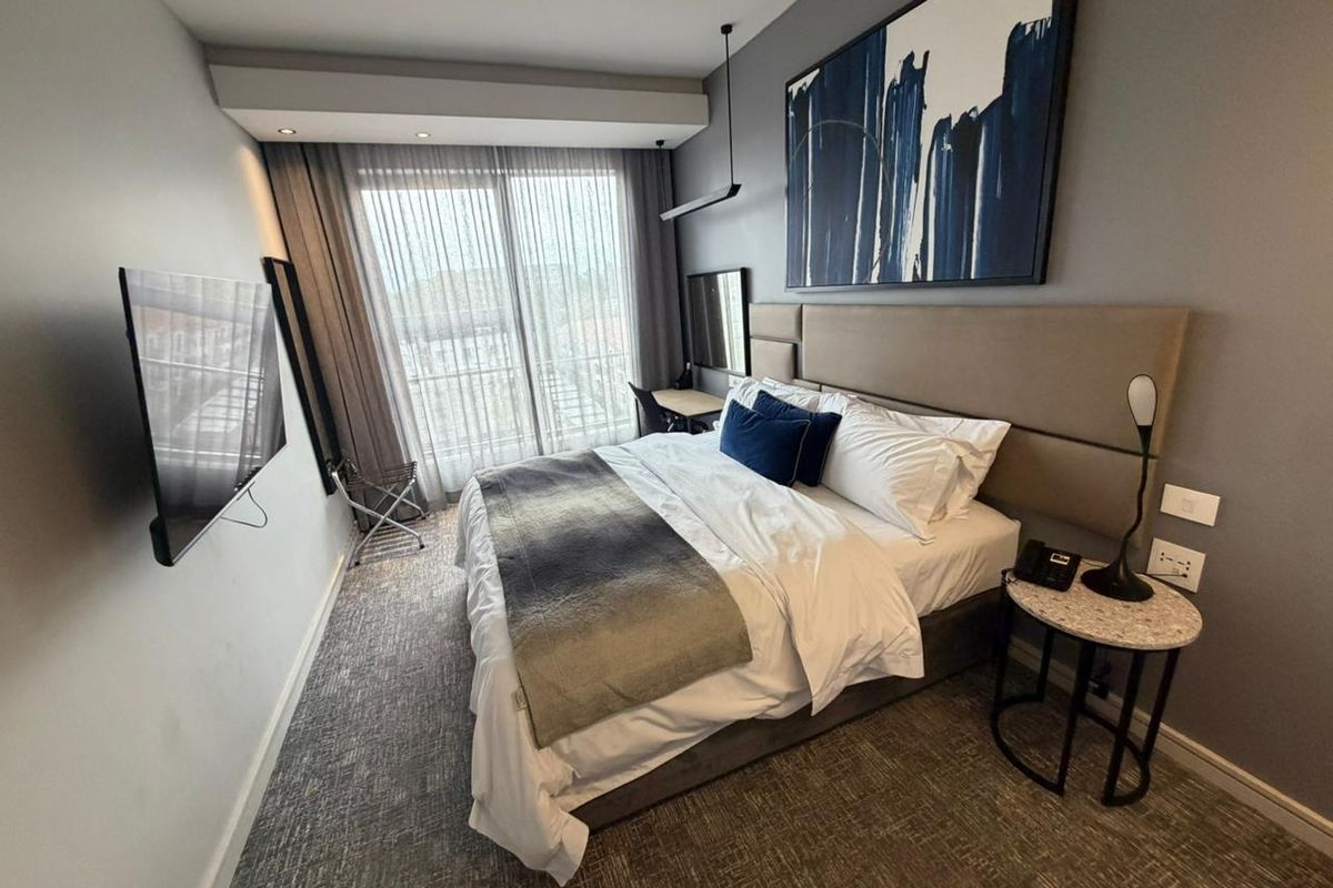 A modern, well-maintained bedroom featuring a built-in headboard, recessed ceiling lighting, and a sliding glass door leading to a balcony.