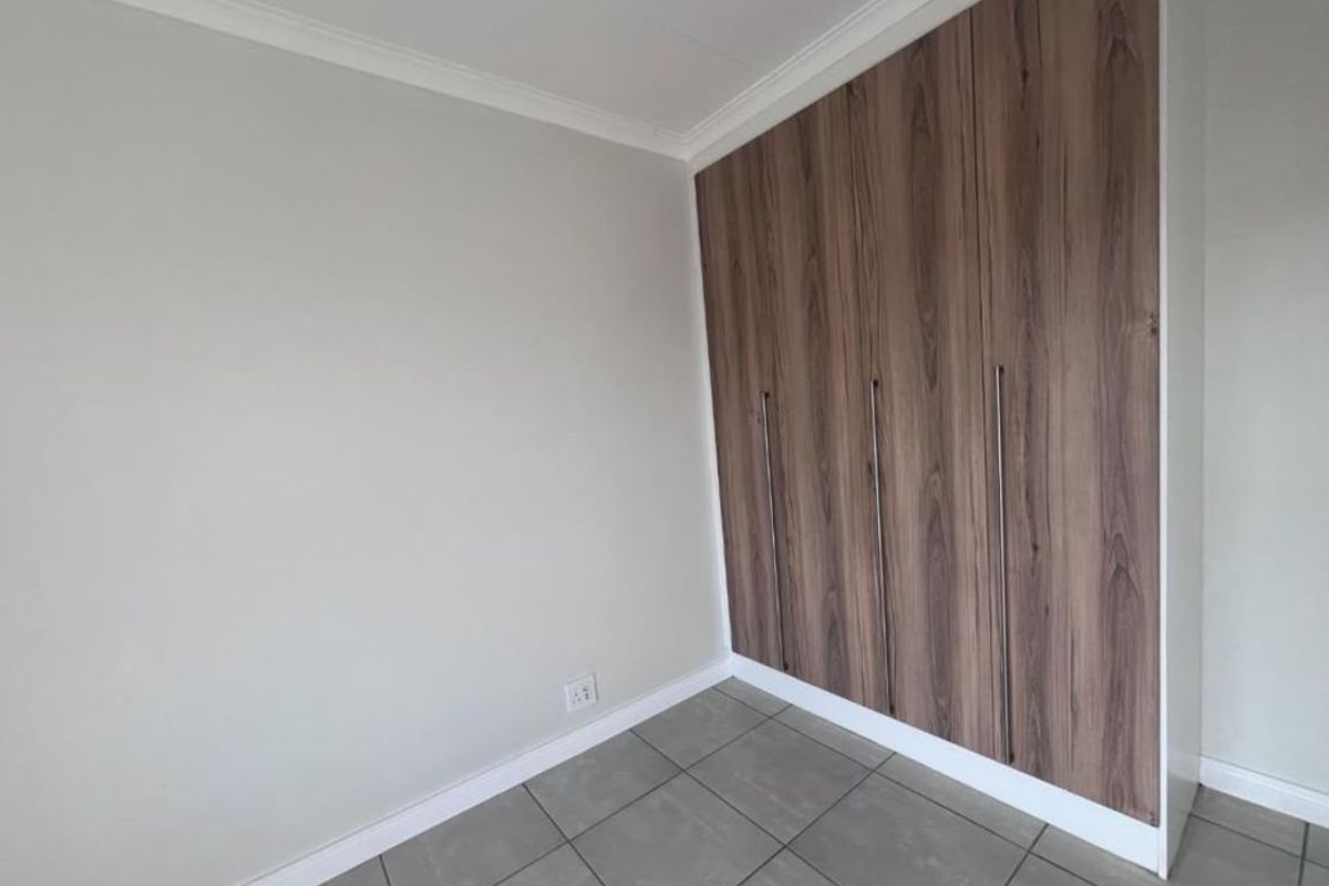 A clean bedroom interior featuring modern wood-finish built-in cupboards and neutral grey floor tiles.