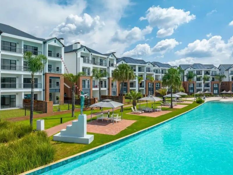 A well-maintained apartment complex featuring a large swimming pool, landscaped gardens, and paved outdoor seating areas for residents.