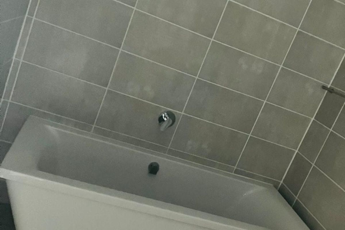 A modern bathroom featuring a white bathtub with wall-mounted chrome fixtures and neutral-toned wall and floor tiling.