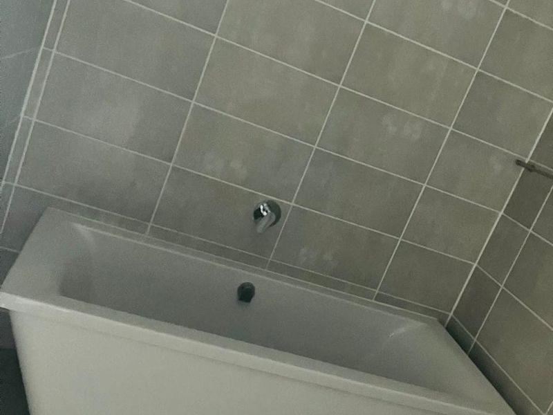 A modern bathroom featuring a white bathtub with wall-mounted chrome fixtures and neutral-toned wall and floor tiling.