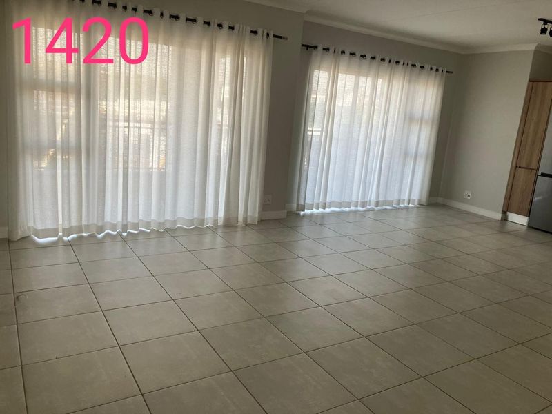 Spacious open-plan living area featuring neutral floor tiles, large sliding glass doors providing natural light, and access to an outdoor balcony.