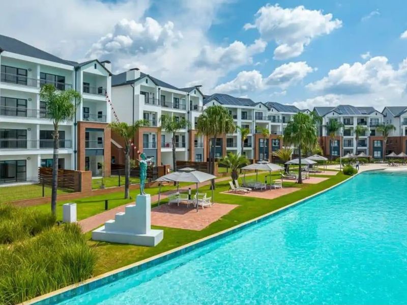 A view of the apartment complex featuring a large swimming pool, landscaped garden areas, and modern multi-story residential buildings with balconies.