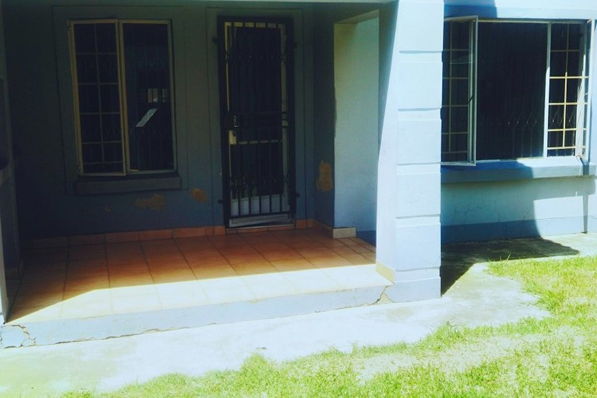 A covered entrance patio featuring tiled flooring, security gate, and exterior wall access, showing signs of wear and paint deterioration.