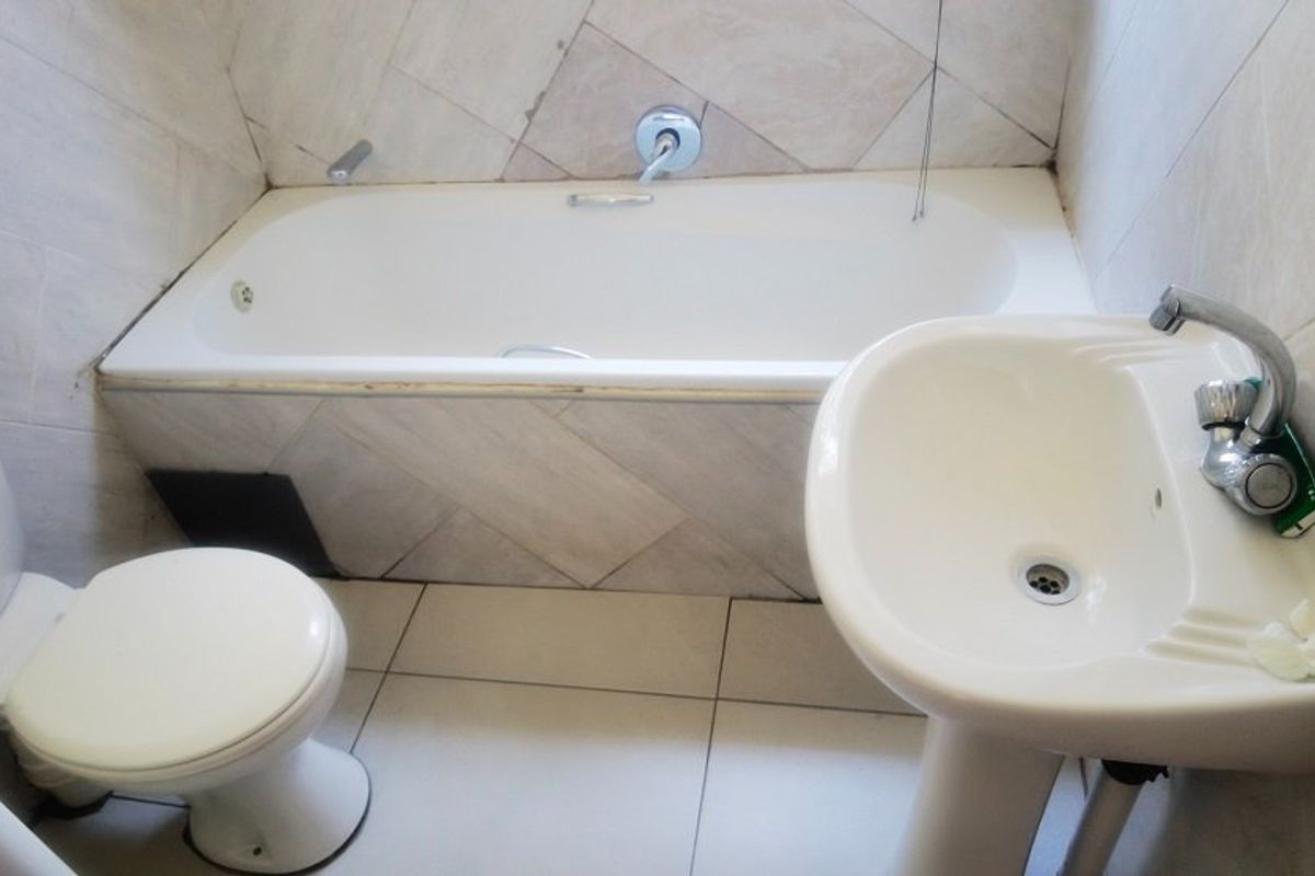 A compact bathroom featuring a standard bathtub, pedestal basin, and toilet with tiled walls and flooring.