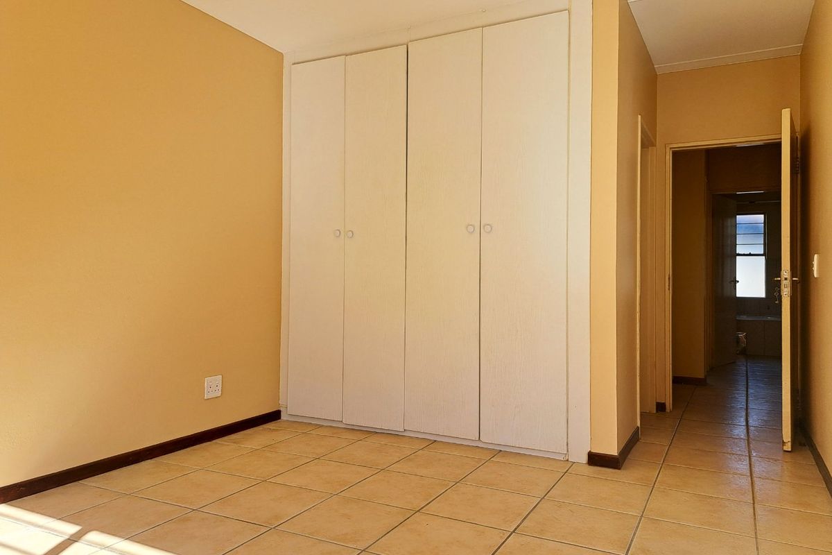 A vacant bedroom featuring built-in cupboards, tiled flooring, and neutral wall tones, offering a clean and functional space.