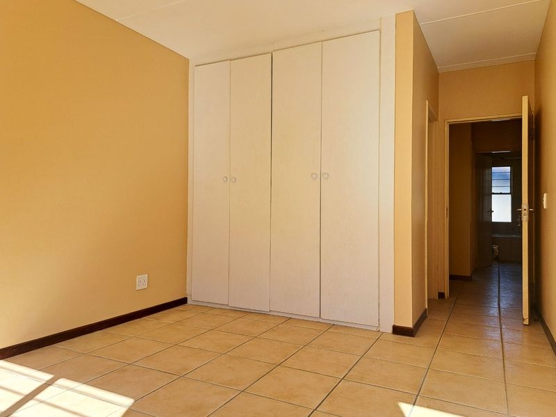 A vacant bedroom featuring built-in cupboards, tiled flooring, and neutral wall tones, offering a clean and functional space.