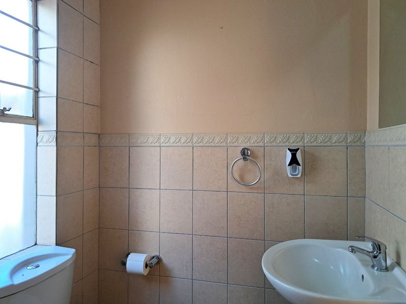 A functional bathroom featuring tiled walls with a decorative border, a pedestal basin with chrome tapware, and a standard toilet.