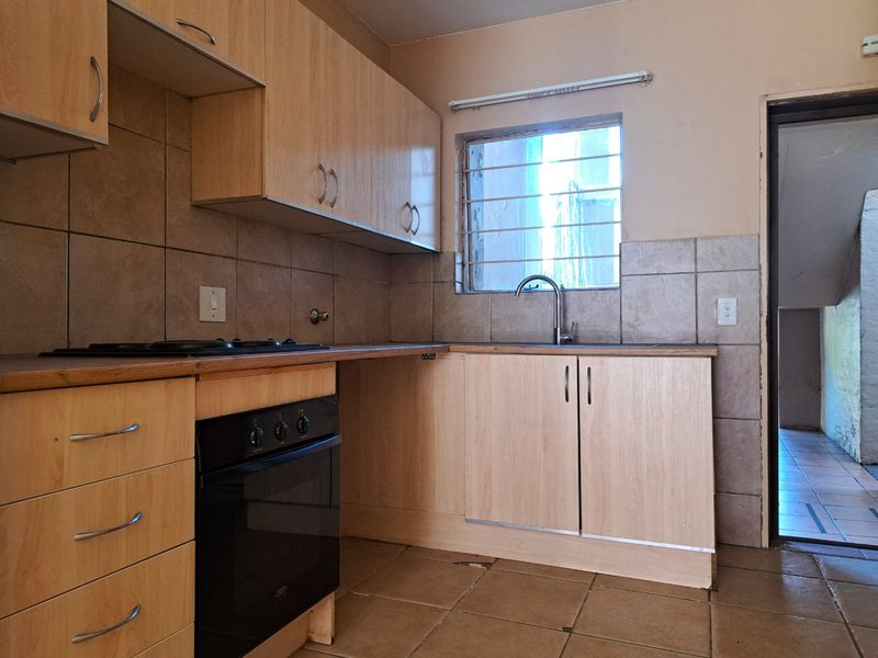 A functional kitchen featuring light wood-finish cabinetry, a built-in oven and hob, tiled backsplash, and a single basin sink with a window view.