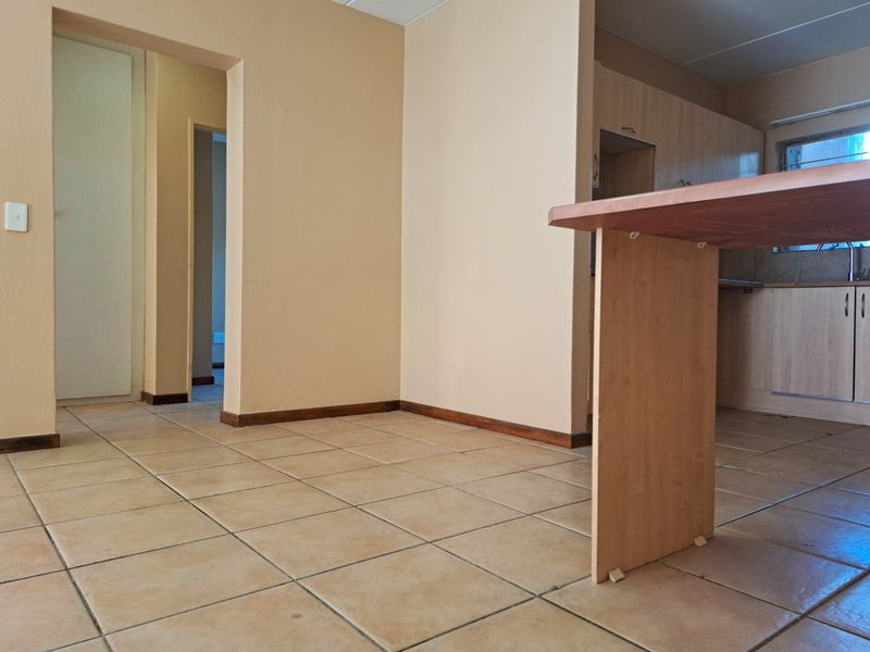 An open-plan living and kitchen area featuring tiled flooring, built-in kitchen cabinetry, and a breakfast counter, leading to a hallway.