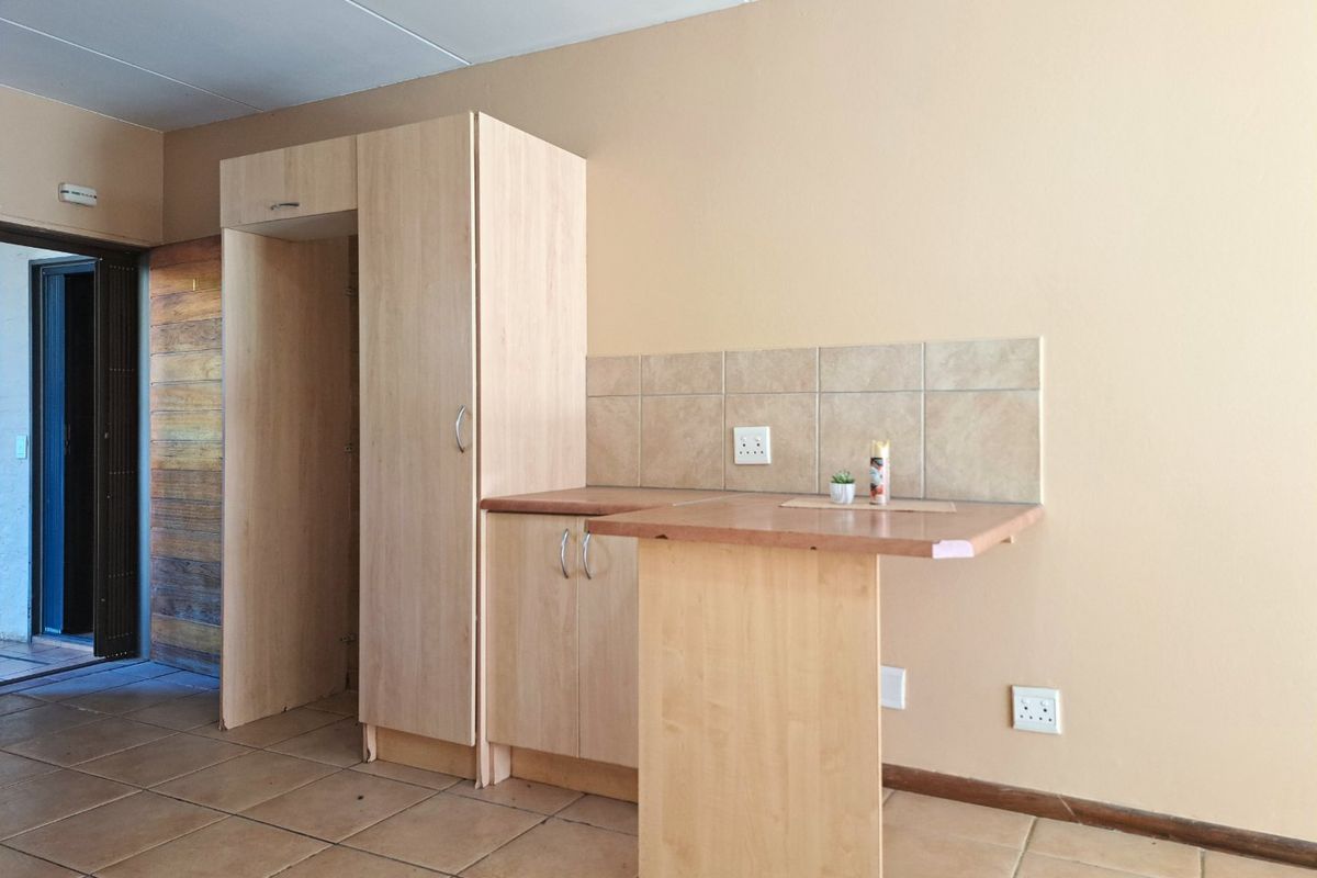 A compact kitchen area featuring light wood-finish cabinetry, tiled backsplash, and a small integrated breakfast bar, set against a neutral wall.