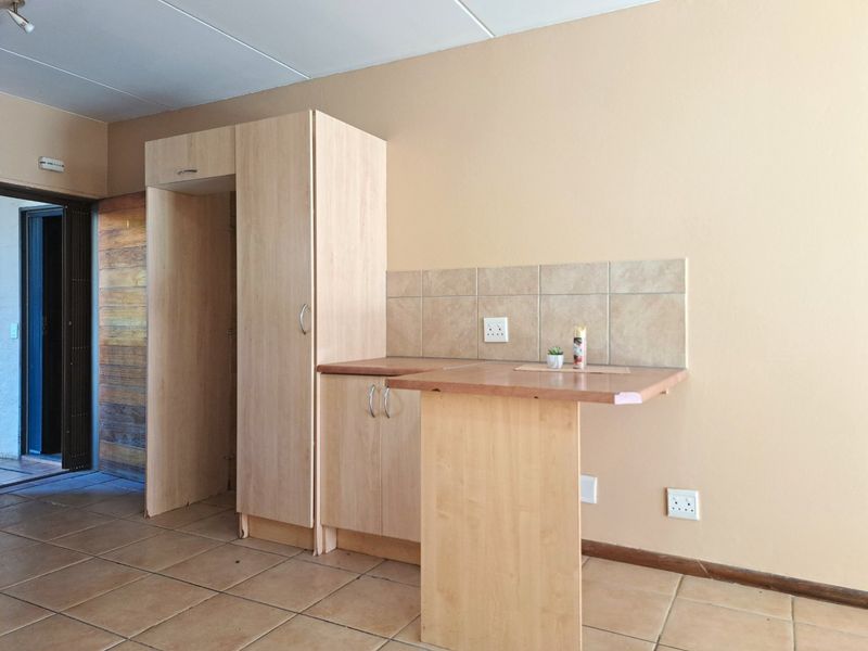 A compact kitchen area featuring light wood-finish cabinetry, tiled backsplash, and a small integrated breakfast bar, set against a neutral wall.