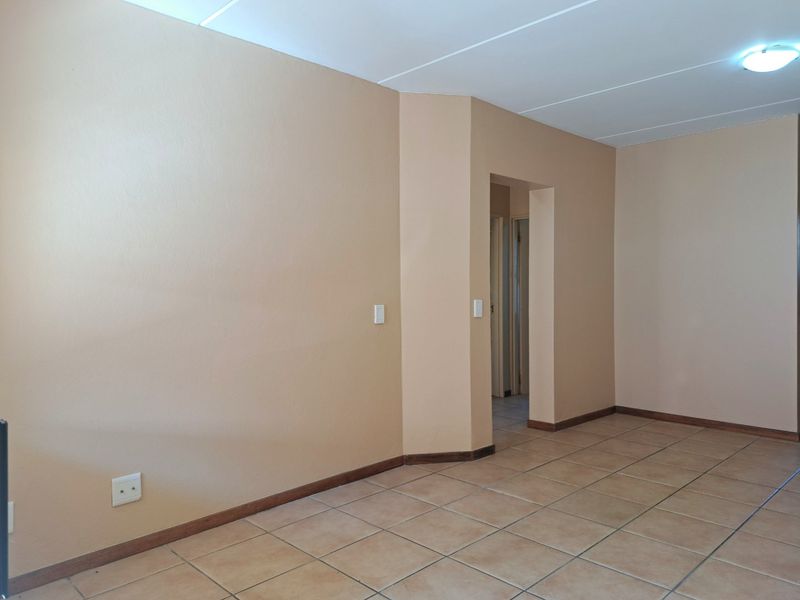 An empty living area featuring neutral wall tones, tiled flooring, and a doorway leading to an adjacent hallway.
