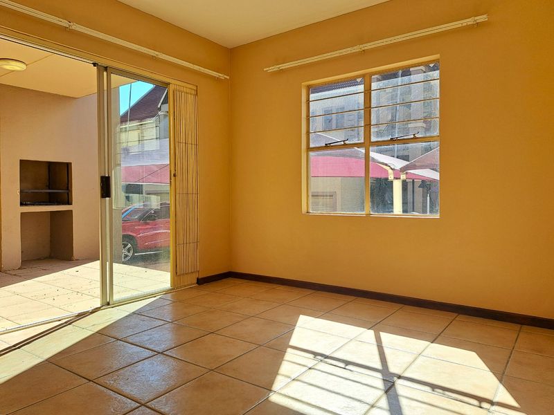 An empty living area featuring tiled flooring, large windows, and sliding glass doors that open onto a patio with a built-in braai.