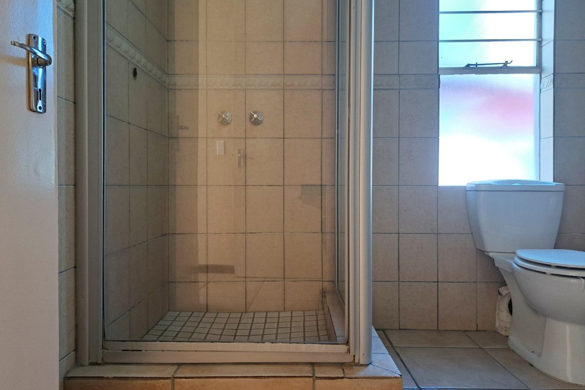 A functional bathroom featuring a tiled shower enclosure with a glass door and a standard toilet, finished with neutral wall and floor tiles.