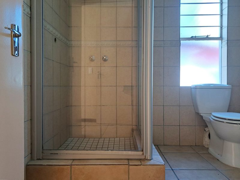 A functional bathroom featuring a tiled shower enclosure with a glass door and a standard toilet, finished with neutral wall and floor tiles.