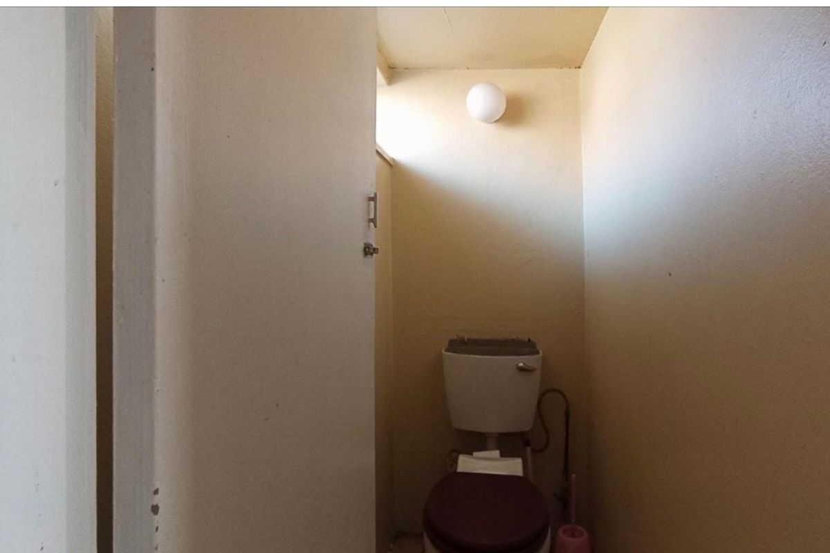 A compact, dated bathroom featuring a standard toilet fixture and basic wall-mounted lighting in a neutral finish.