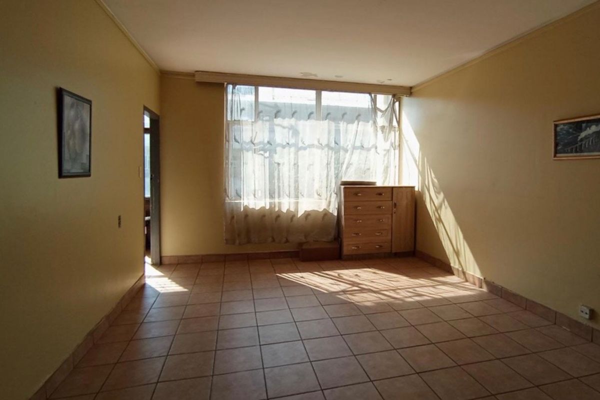 A spacious living area featuring tiled flooring and large windows that provide natural light, offering a blank canvas for renovation or restyling.