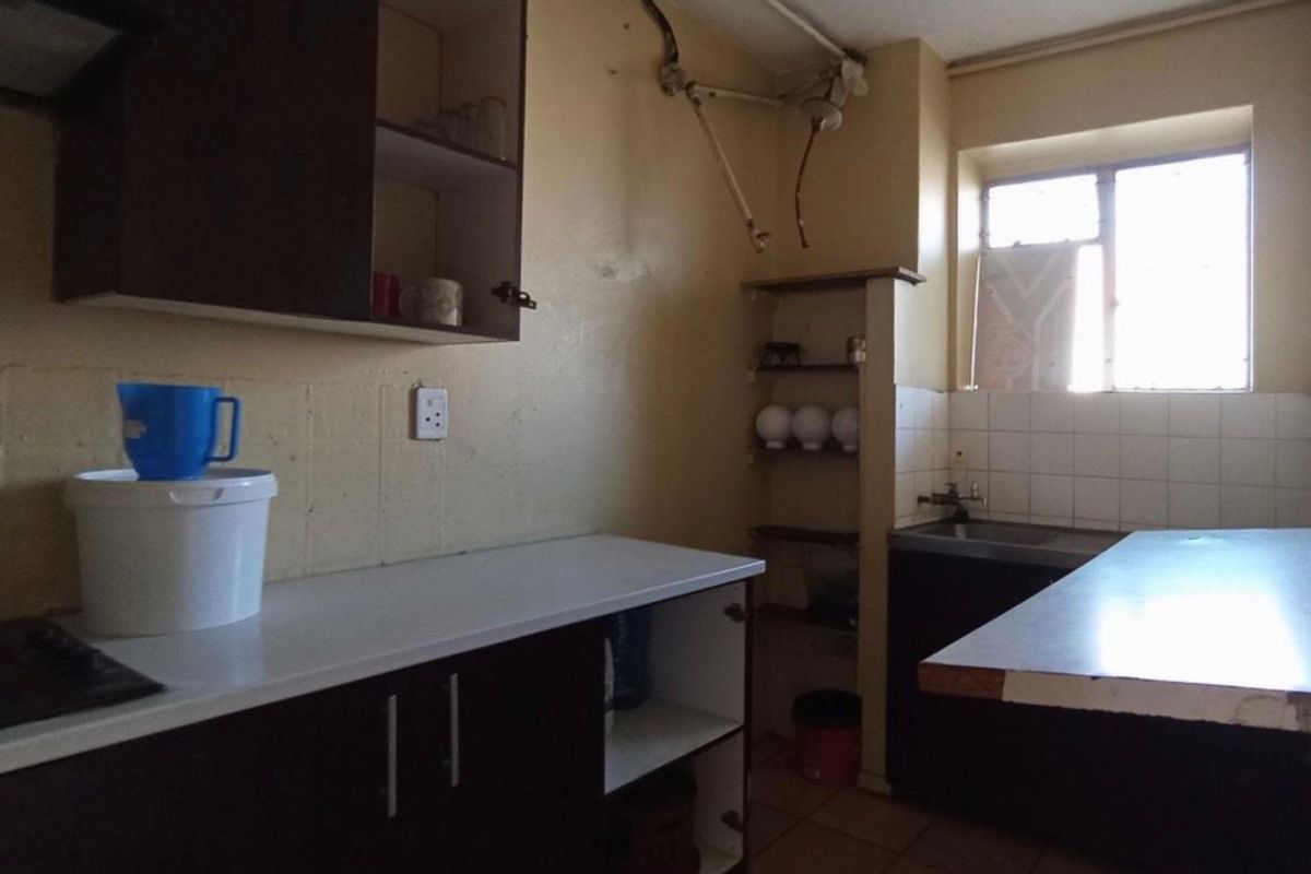 A dated kitchen featuring basic cabinetry, a stainless steel sink, and tiled splashbacks, requiring significant renovation and cosmetic updates.