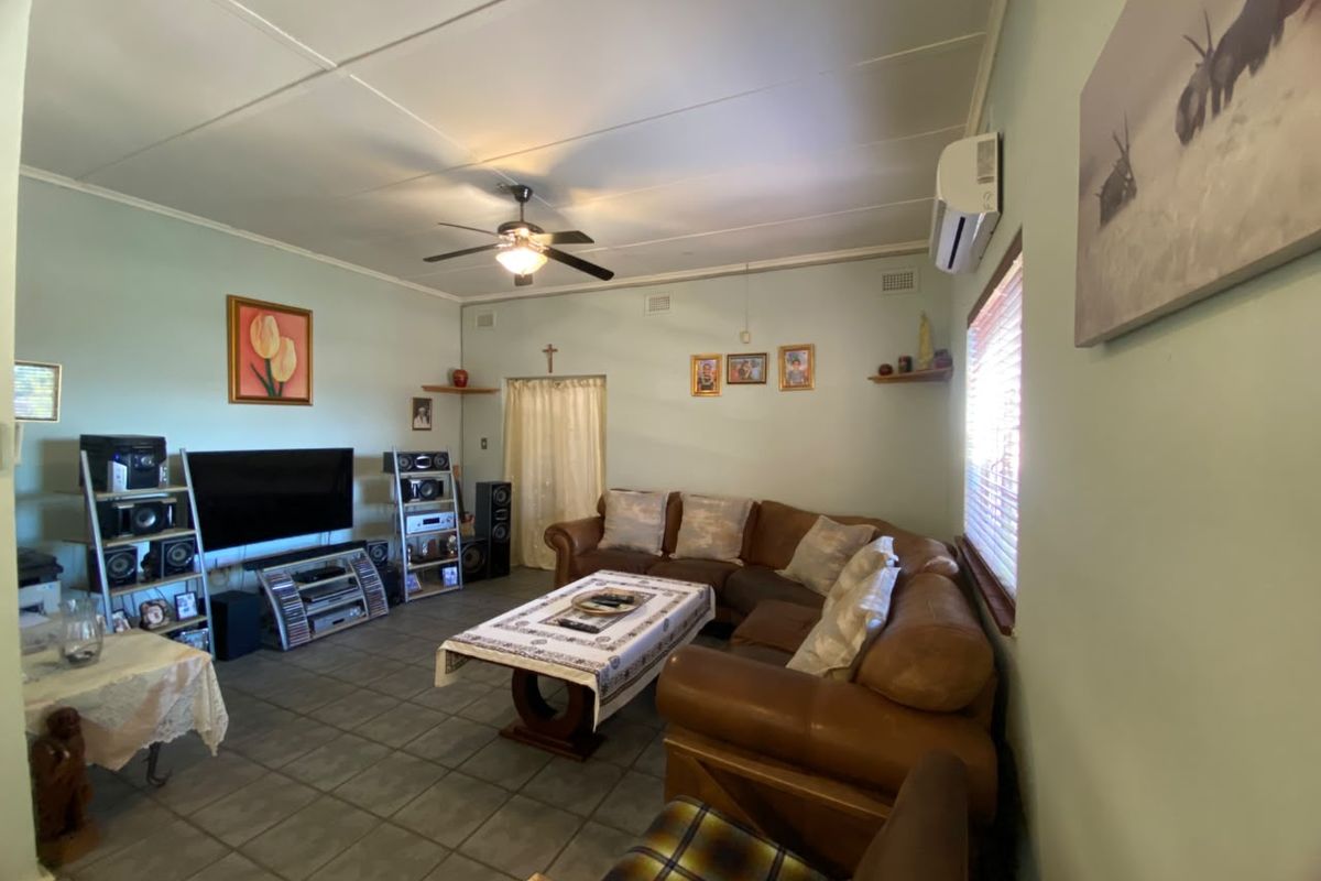 A spacious living room featuring tiled flooring, a ceiling fan, and a wall-mounted air conditioning unit.