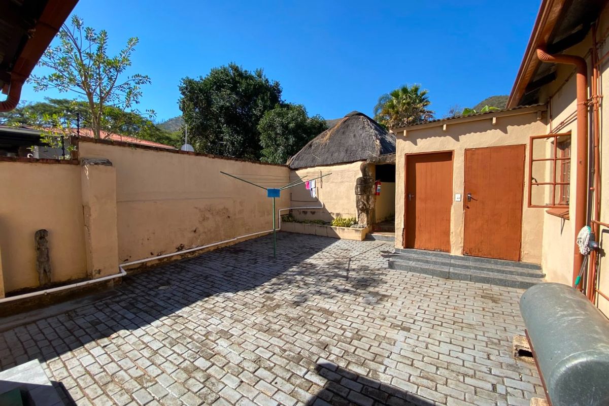 A paved rear courtyard area featuring exterior access doors, a perimeter wall, and a small thatched structure in the background.