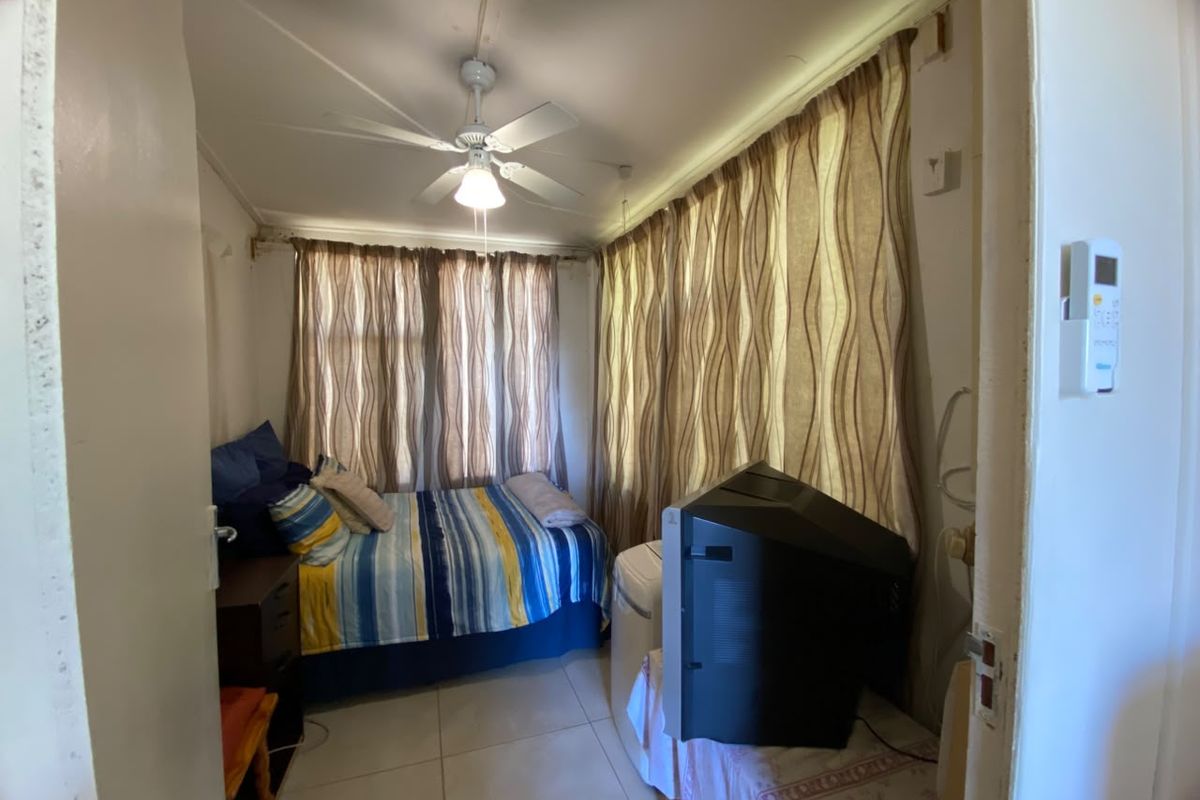 A compact bedroom featuring tiled flooring, a ceiling fan, and large windows with curtains, providing a functional sleeping space.