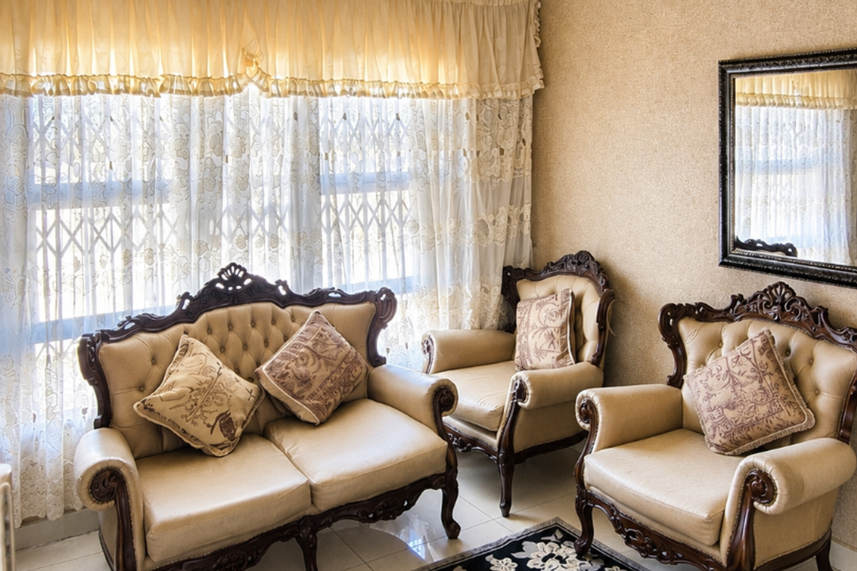 A formal living room featuring classic ornate ceiling rose, decorative cornice, and large window with security gate.