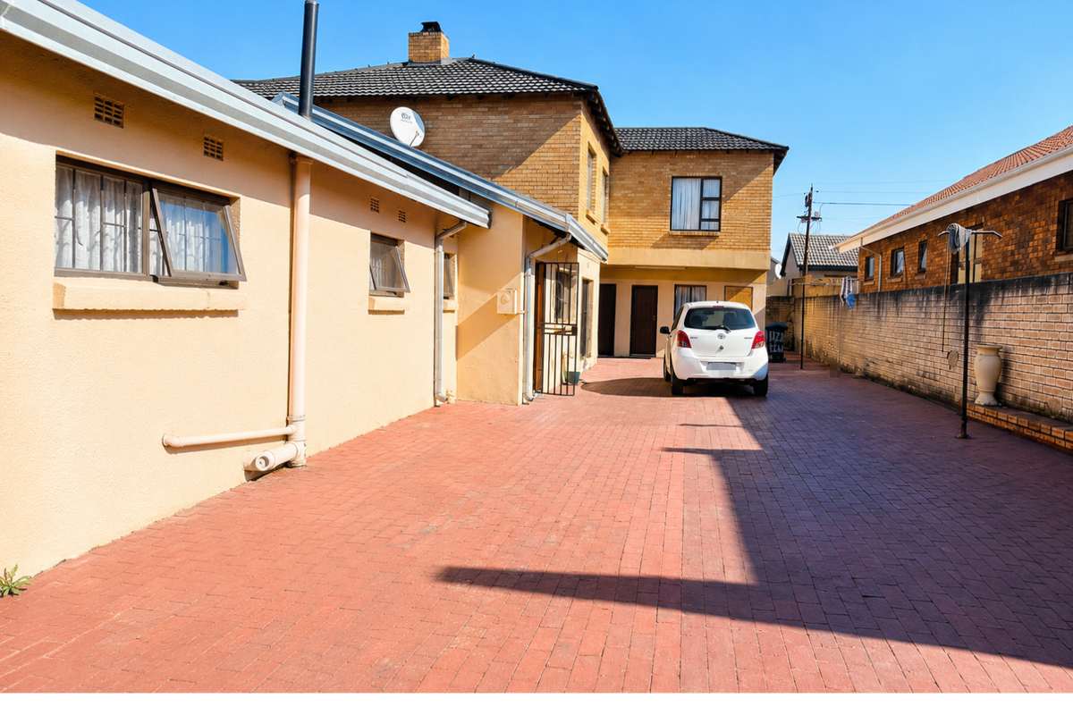Exterior view of the property showing a paved driveway, brick boundary wall, and multi-level building facade with tiled roof.