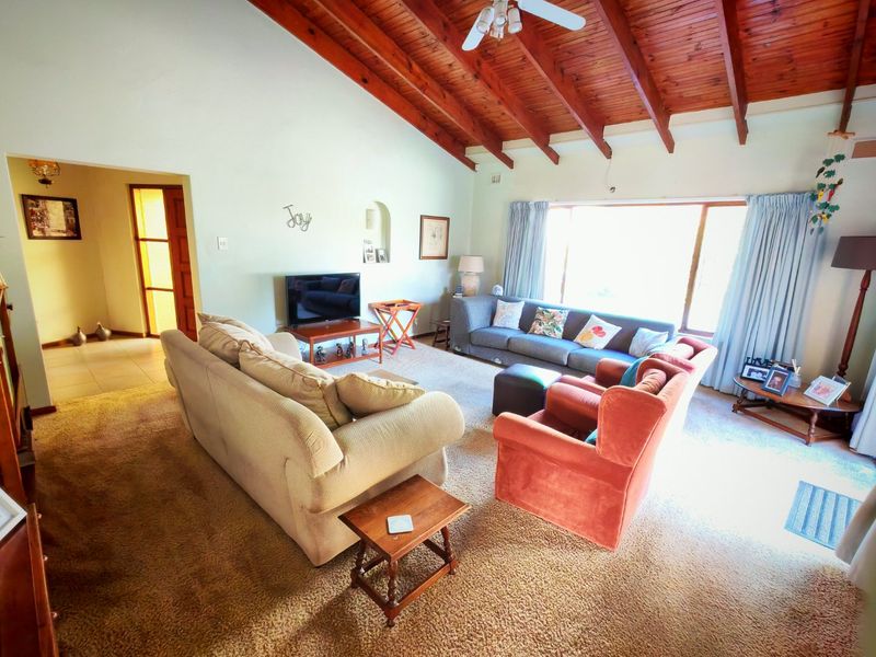 Spacious living room featuring a high vaulted timber-beamed ceiling, large windows for natural light, and neutral wall finishes.
