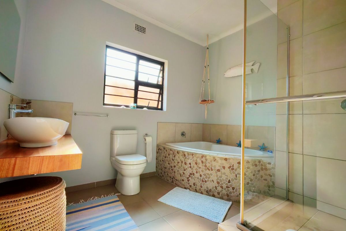 A functional bathroom featuring a vessel sink, a built-in bathtub with pebble-tiled surround, and a separate glass-enclosed shower.