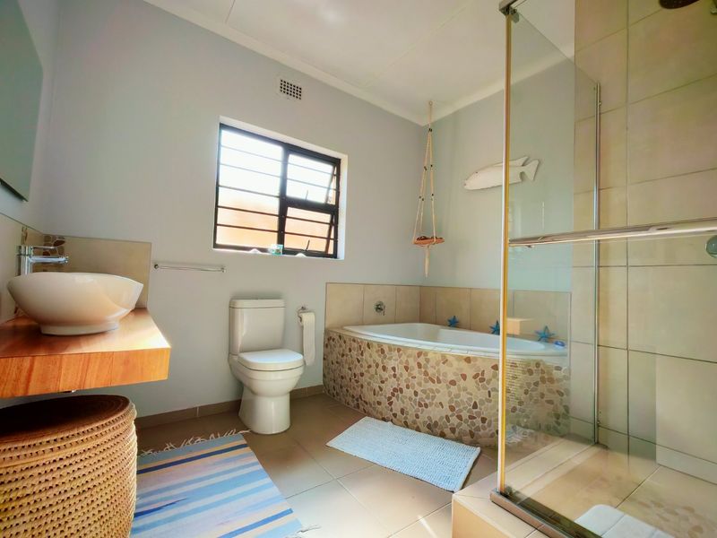 A functional bathroom featuring a vessel sink, a built-in bathtub with pebble-tiled surround, and a separate glass-enclosed shower.