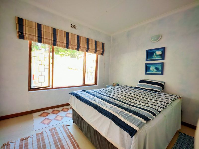 A bedroom featuring a large window with security bars, wall-mounted lighting, and a neutral painted finish.