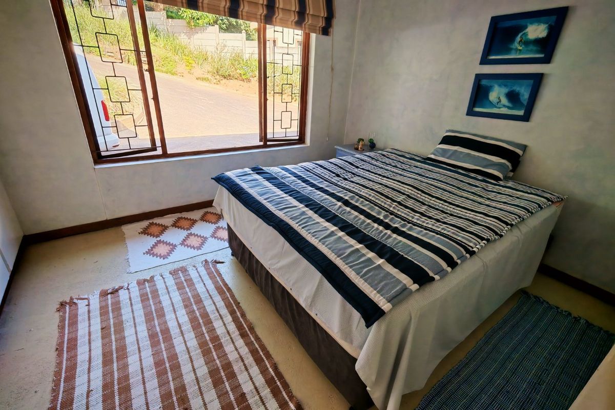 A bedroom featuring a large window with security bars, neutral wall finishes, and concrete flooring.