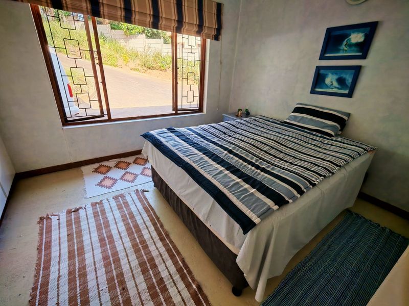 A bedroom featuring a large window with security bars, neutral wall finishes, and concrete flooring.