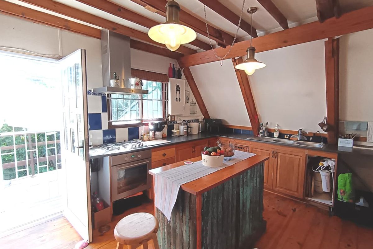 Rustic kitchen featuring exposed timber beams, wooden cabinetry, a central island, and direct access to an outdoor balcony area.