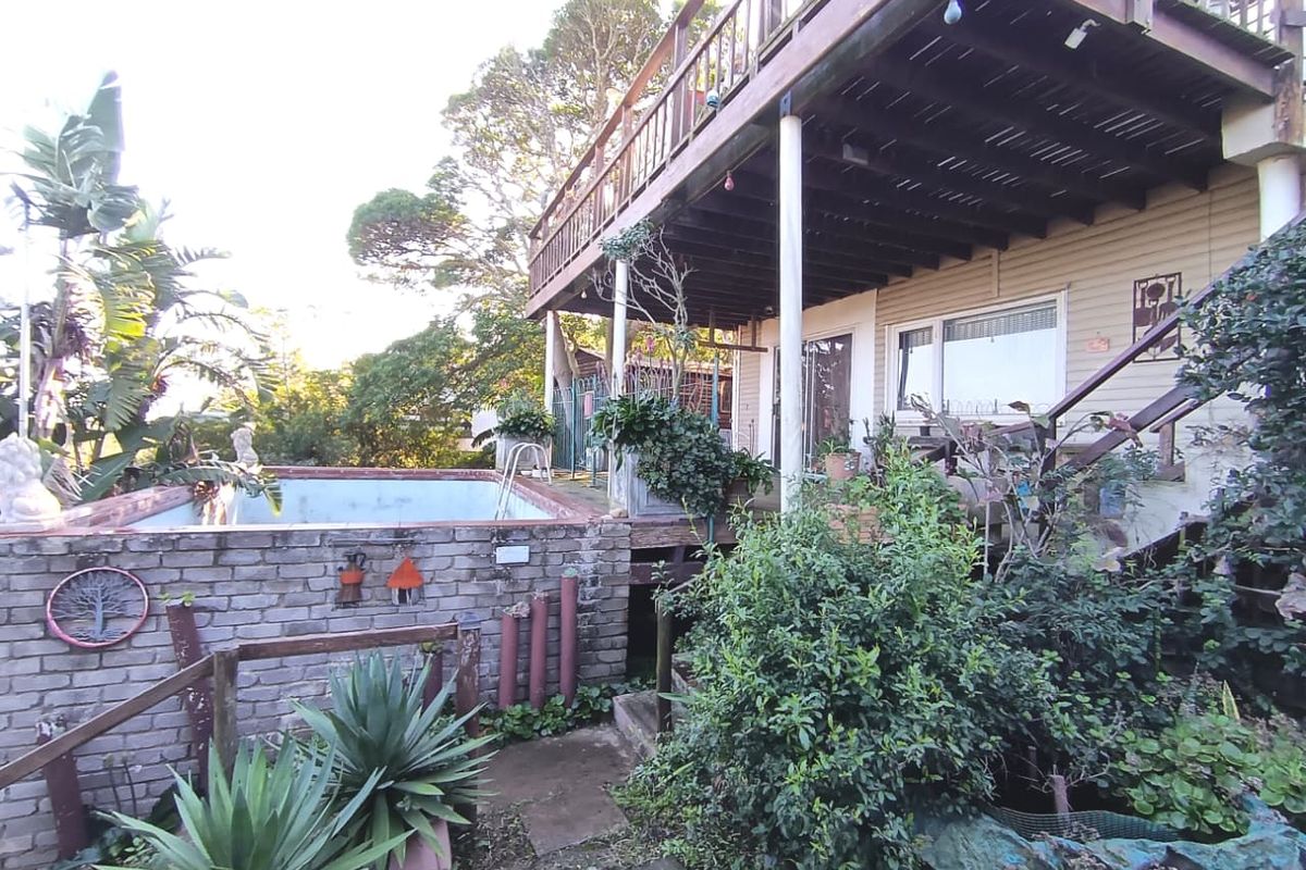 Rear exterior view featuring a raised timber deck, a brick-surrounded swimming pool, and established garden landscaping.