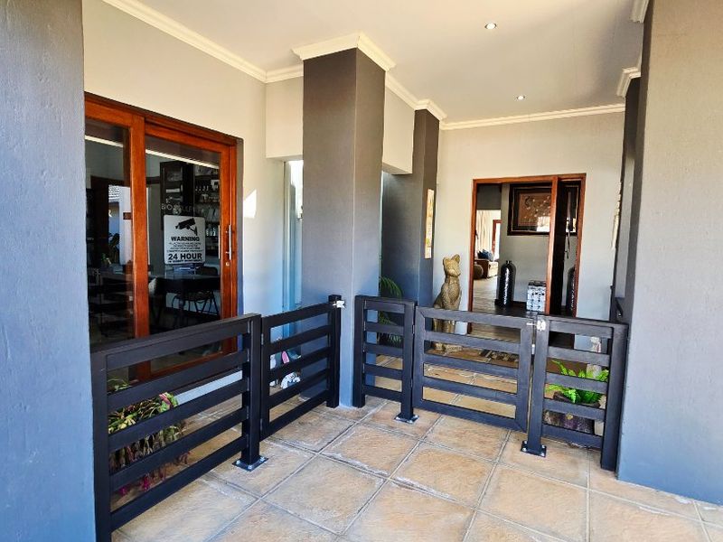A covered patio area featuring tiled flooring, recessed downlighting, and a black metal safety gate, providing access to the home's interior.
